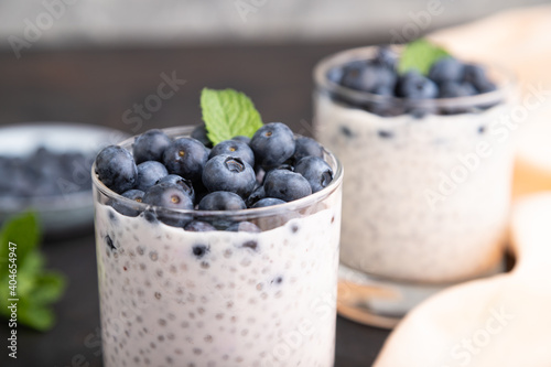 Yogurt with blueberry and chia in glass on black concrete background. Side view, close up.