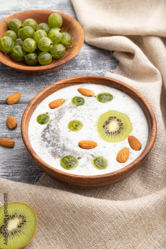 Yogurt with kiwi, gooseberry, chia and almonds in wooden bowl on gray wooden background. Side view, close up.