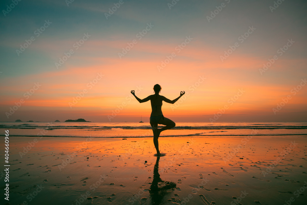 An woman practicing yoga on the ocean side, the silhouette of awesome sunset.