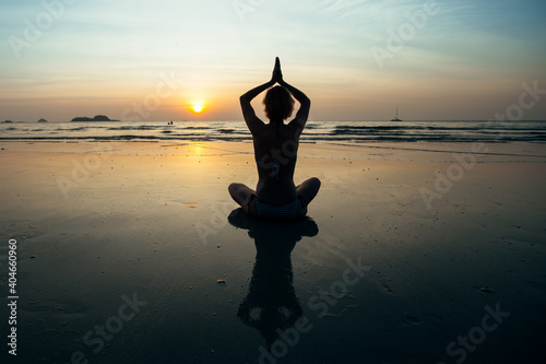 Yoga woman meditation on sunset coast with reflection in water.