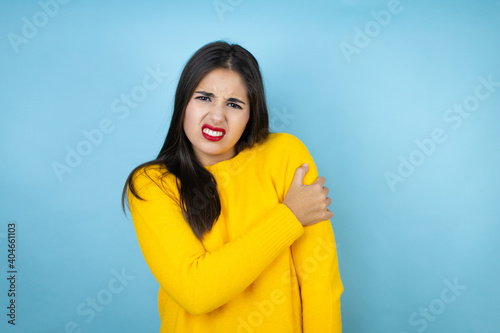 Young beautiful woman wearing yellow sweater over isolated blue background with pain on her shoulder and a painful expression