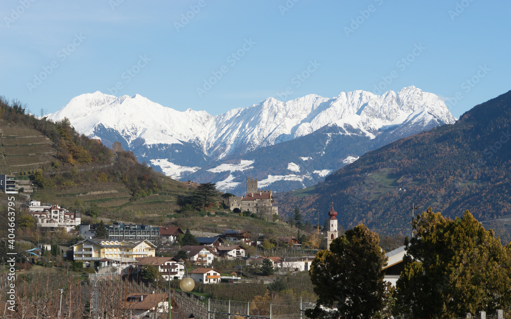 Fototapeta premium Picturesque mountain landscape in Naturns in South Tyrol in autumn, in the fore an old church, castle and old buildings and in the background the snow-covered Alps, no people