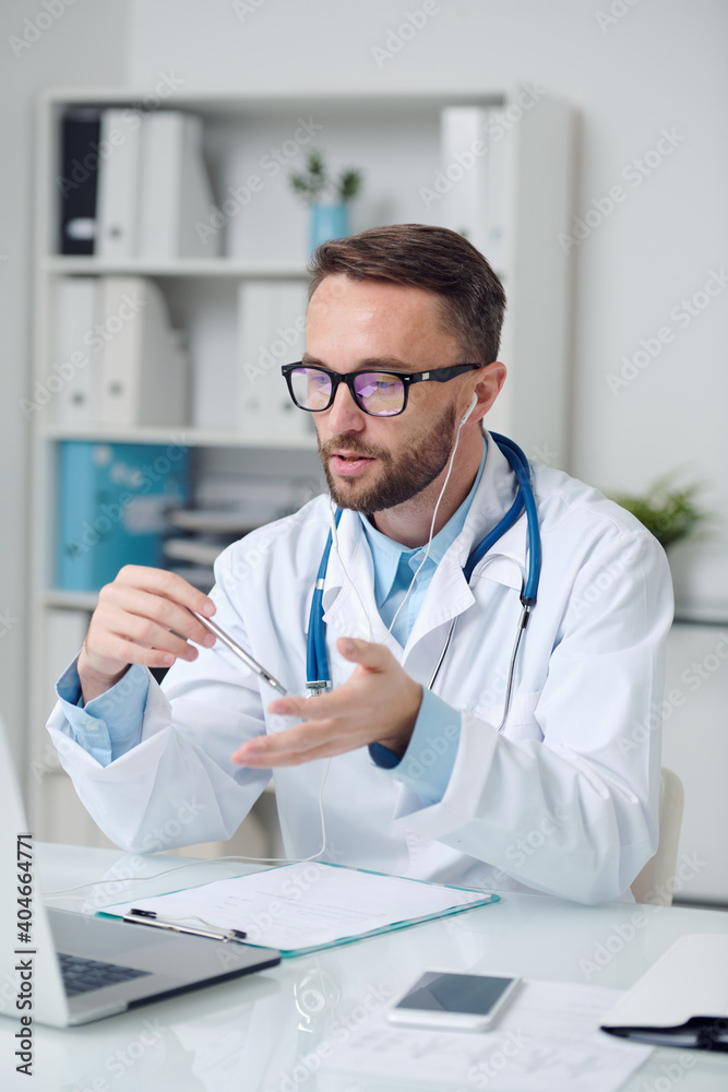 Young male doctor in eyeglasses and earphones giving medical recommendations Young male doctor in eyeglasses and earphones giving medical recommendations