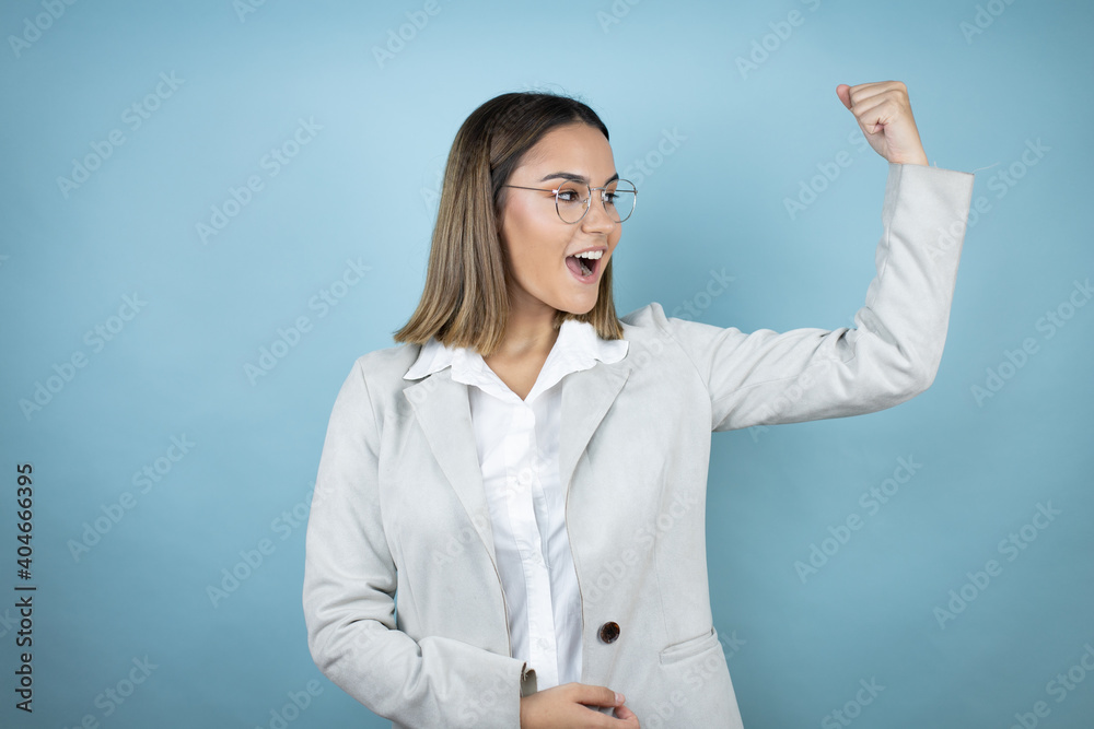 Young business woman over isolated blue background showing arms muscles smiling proud