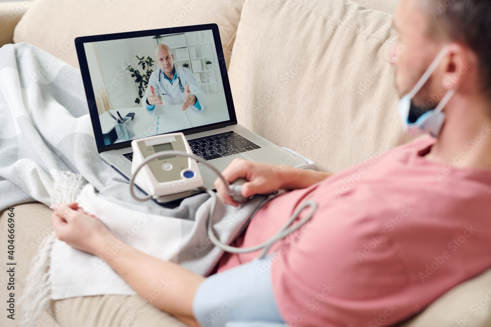 Confident doctor on laptop screen giving medical recommendations to sick man Confident doctor on laptop screen giving medical recommendations to sick man