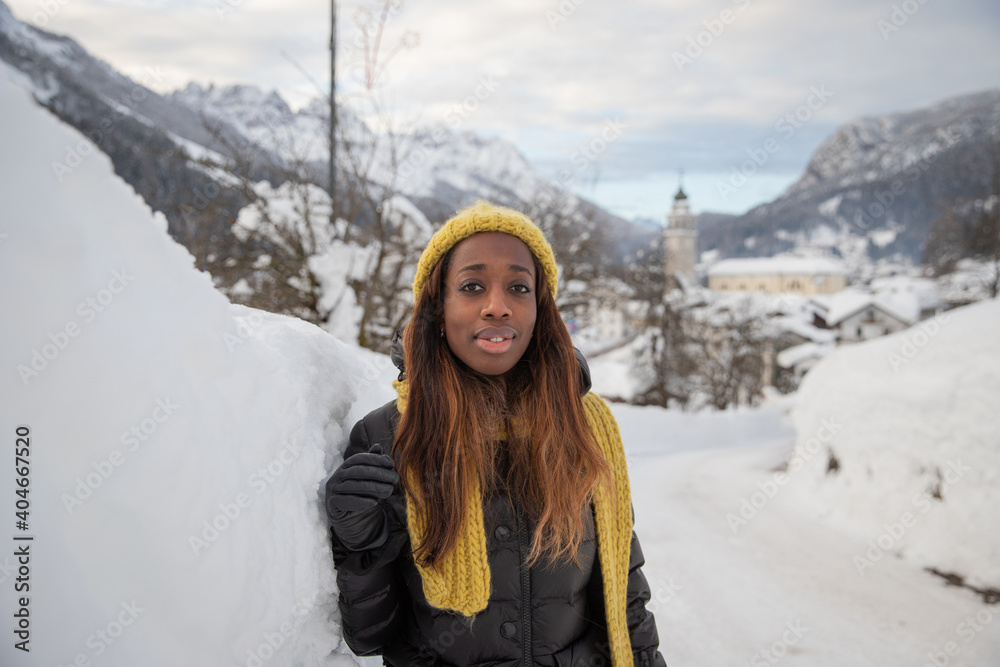 An African girl dressed heavily to withstand the cold, poses near a snow wall in the mountains.