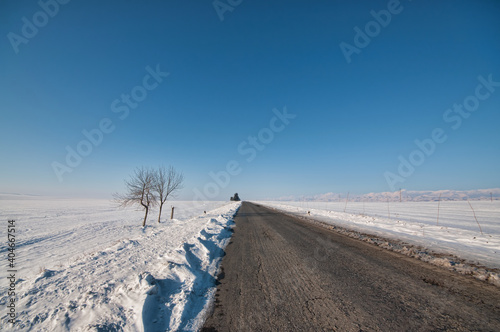 Countryside road through winter field covered in snow. Clear asphalt road.