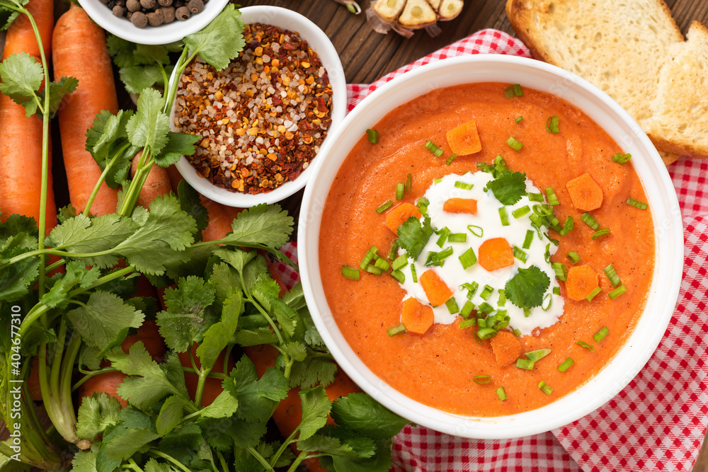 Carrot soup of freshly ground carrots with herbs and sour cream on a wooden background. Carrot soup of freshly ground carrots with herbs and sour cream on a wooden background.