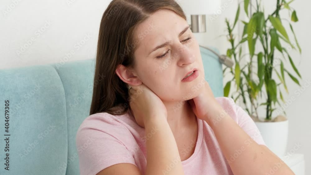Portrait of young brunette womnan massaging her aching neck after feeling pain Portrait of young brunette womnan massaging her aching neck after feeling pain