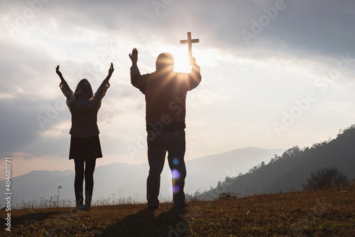 Easter Sunday concept: Silhouette man and child praying to the GOD while holding a crucifix of Jesus Christ on autumn sunrise background