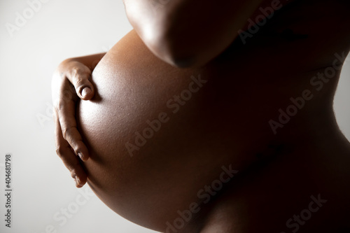 Beautiful African American heavily pregnant woman.  Close up of belly in naked profile with studio lighting on white background . Vertical format
