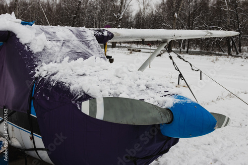 Gray blade, the hood of a small private plane covered with snow, winter in bad weather at the airport.
