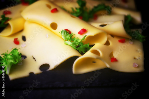 Slices of hard maasdam cheese on a dark background. Cheese with holes.