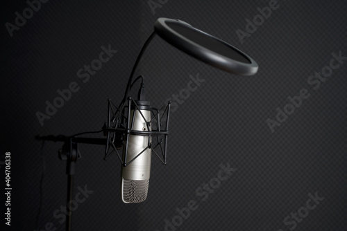 Closeup microphone on a stand in front of black soundproof wall in professional recording studio. © chadchai