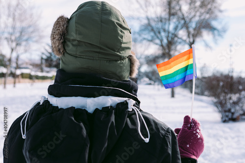 Obraz na plátně Lesbian woman from behind wearing a hair snow cap, in a snowy area holding lgbt