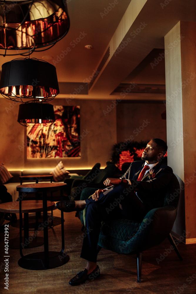 Successful business man sit in a bar, planing new deal or project, smiling. Handsome African American male boss show confidence and success. Influential leader of company wearing stylish formal suit Successful business man sit in a bar, planing new deal or project, smiling. Handsome African American male boss show confidence and success. Influential leader of company wearing stylish formal suit