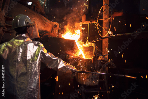 Smelting of metal in large foundry. Iron and steel being melted in furnace. Worker controlling metallurgy process of molten iron. Hot steel pouring in production plant.