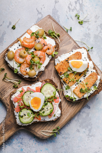 Variety of sandwiches for breakfast, snack, appetizers - tempeh, salmon, prawns grilled whole grain bread sandwiches with microgreens on a light background