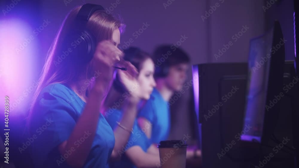 Group of friends sitting in the gaming club and having an online gaming tournament - woman putting on her headphones and joins the game Group of friends sitting in the gaming club and having an online gaming tournament - woman putting on her headphones and joins the game