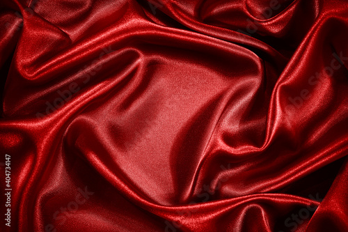 Red silk satin background. Shiny fabric with wavy soft pleats. Beautiful fabric background with empty space for your product and design.