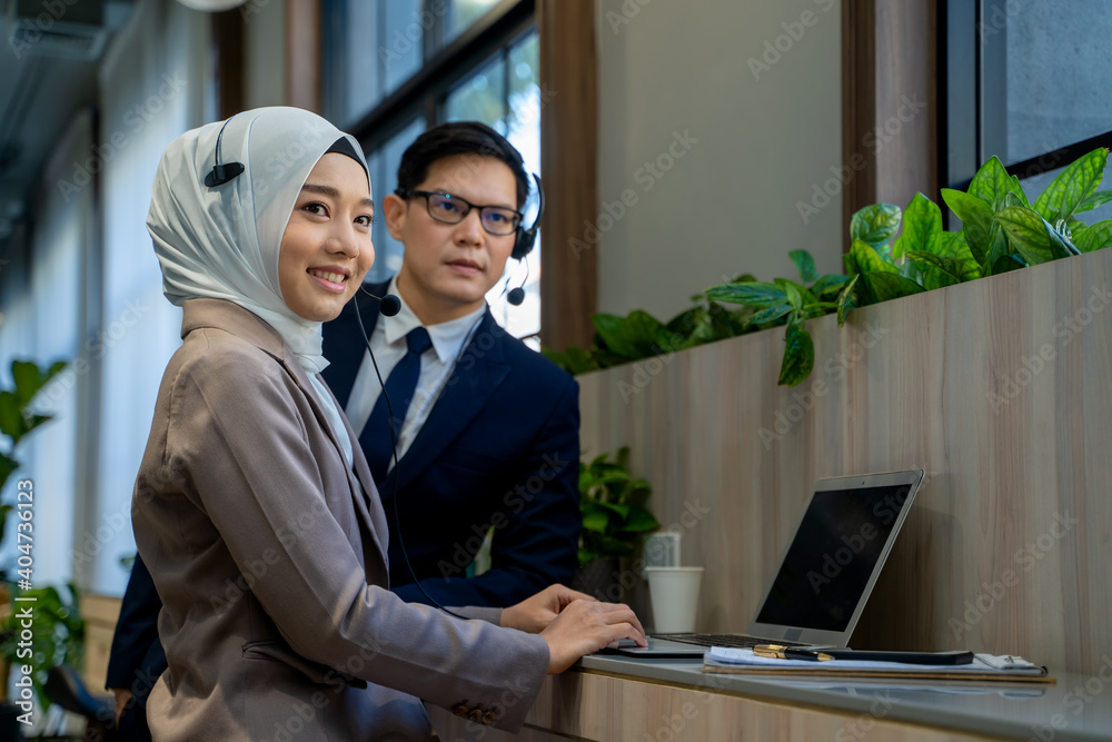 Businessman and Muslim lady employee with headset use laptop working in office.Work concept of diversity of culture different race type of people co-working together