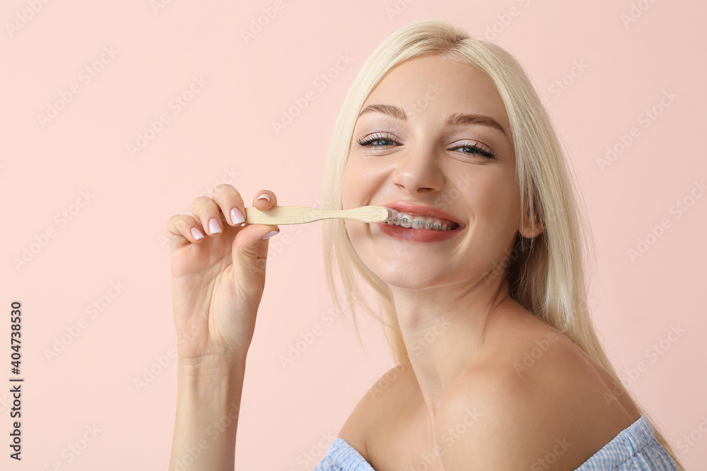 Young woman with dental braces and wooden toothbrush on color background Young woman with dental braces and wooden toothbrush on color background