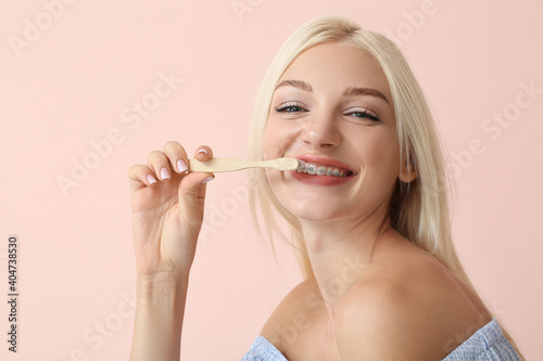 Young woman with dental braces and wooden toothbrush on color background