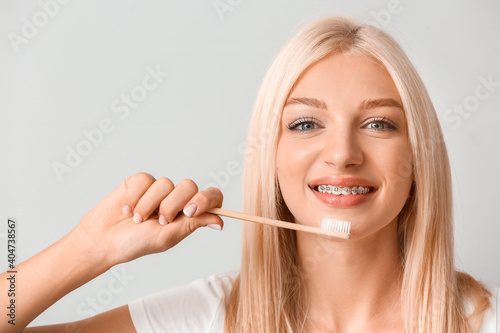 Young woman with dental braces and wooden toothbrush on light background