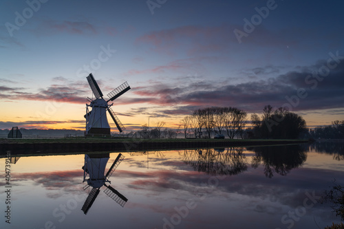 Foggy dawn at a windmill reflected in a canal during winter.