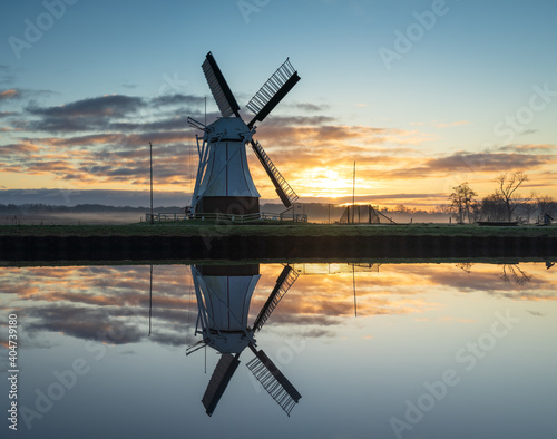 A tranquil winters dawn at a windmill reflected in a canal. © sanderstock