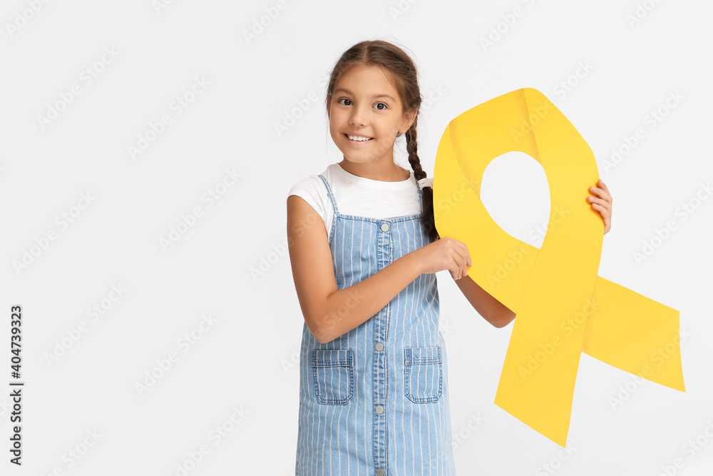 Little girl with golden ribbon on light background. Childhood cancer awareness concept