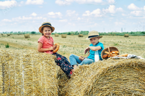 Happy children having breakfast with milk and bread in the countryside sitting on a wheat stack Happy childhood concept