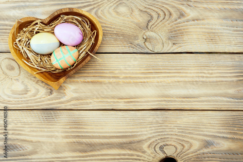 Colorful easter eggs in a wooden plate on a wooden background with place for text, top view
