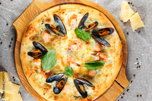 classic italian pizza with shrimp seafood, mussels and parmesan cheese and basil leaves on a wooden board on a parchment background with cheese