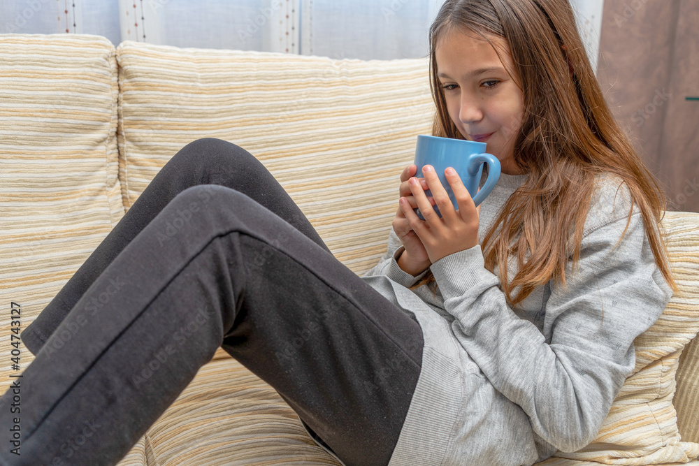 Pretty little girl having a cup of milk for breakfast on the sofa in her living room. Selective focus Pretty little girl having a cup of milk for breakfast on the sofa in her living room. Selective focus