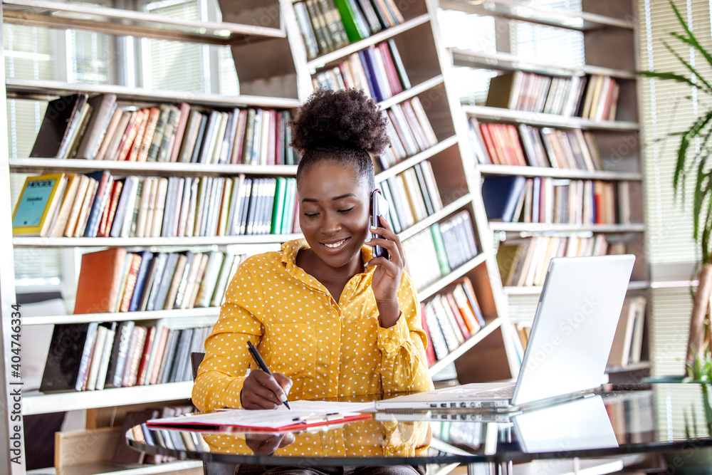 Foto Successful business woman working at the office, African American woman talking on her mobile phone and working on laptop