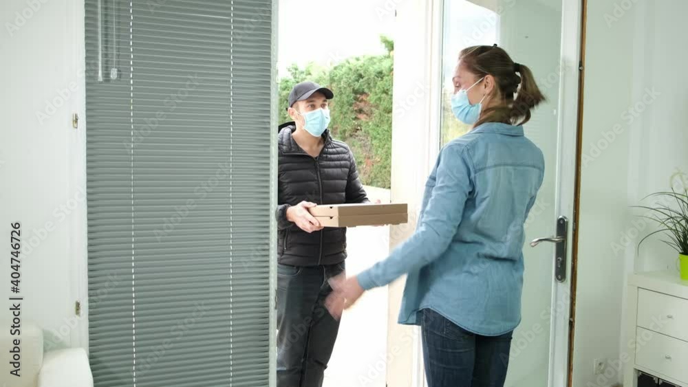 Young pizza delivery man with protection mask delivering pizzas to a beautiful woman at home during covid 19 pandemic Young pizza delivery man with protection mask delivering pizzas to a beautiful woman at home during covid 19 pandemic
