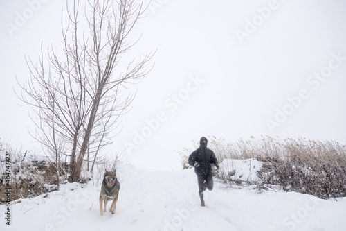 man running with dog in snowy landscape