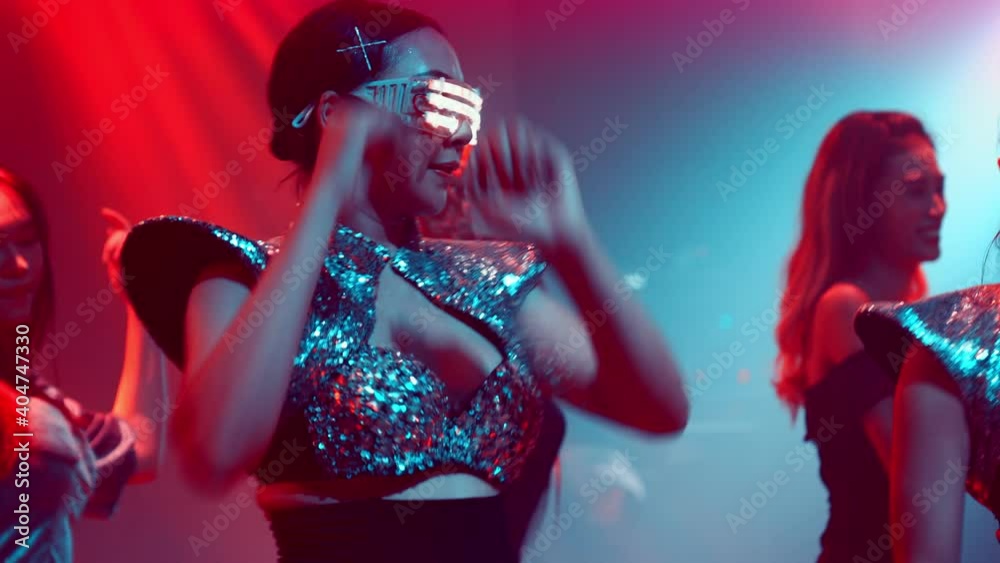 Group of people dance in disco night club to the beat of music from DJ on stage . New year night party and nightlife concept .
