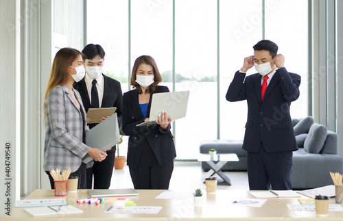 Asian businessman in suit waring a mask, while walking into a group of colleagues. The team is preparing for the meeting. Concept of new normal office business during coronavirus pandemic outbreak.
