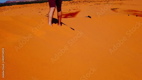 A fit, active man walking across coral sand dunes in Utah, USA, United States of America during summer tourist season on a warm, sunny day.  photo