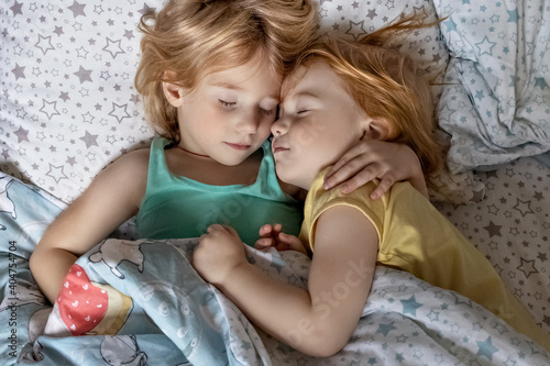Two little sibling girls sisters sleeping in an embrace in bed under one blanket