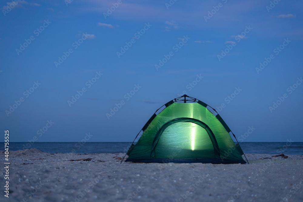 Tent is lit up at night. Camping by the seashore. Active tourism