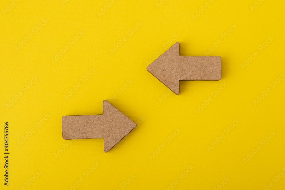 Two wooden arrows on yellow background. Direction signs. Copy space. Mock up - obrazy, fototapety, plakaty 