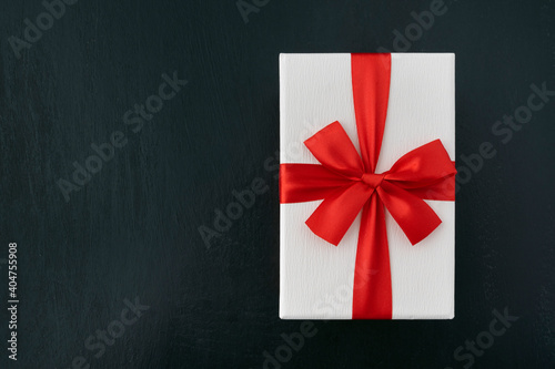 White cardboard box with red ribbon on black background, top view. Gift wrapping. Copy space