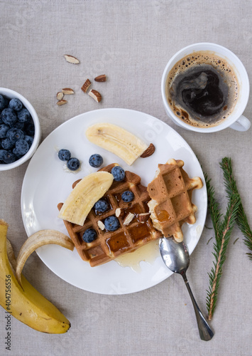 Breakfast with Belgian waffles with honey, blueberries, banana and almonds with a cup of fresh coffee on a linen tablecloth. 