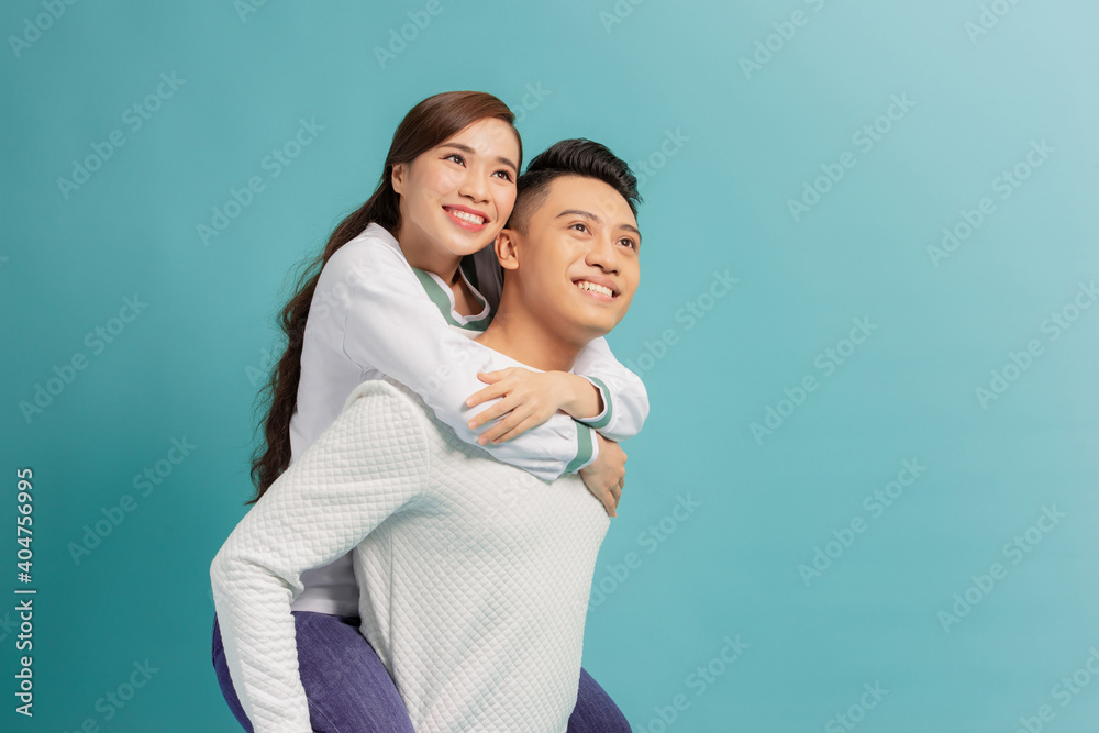 Love forever, fun together. Young handsome boyfriend is piggybacking his cute lover, on blue background Love forever, fun together. Young handsome boyfriend is piggybacking his cute lover, on blue background