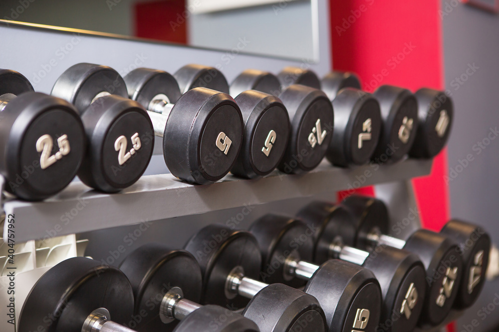 Dumbbells of different weights with numbers are on a rack in the gym. Sports equipment, training, bodybuilding. Background