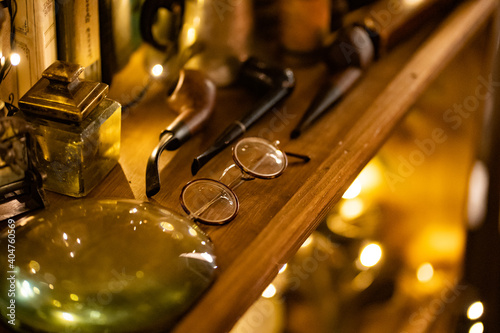 vintage glasses with a round frame on the shelf of a wardrobe with a magnifying glass, a smoking pipe and retro things. collecting antiques. Low light. Selective focus.