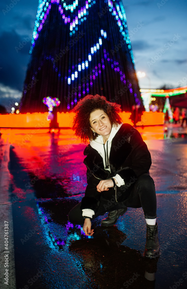 Happy smiling woman posing at night street festive square. Christmas, New Year celebration, winter holidays conception.